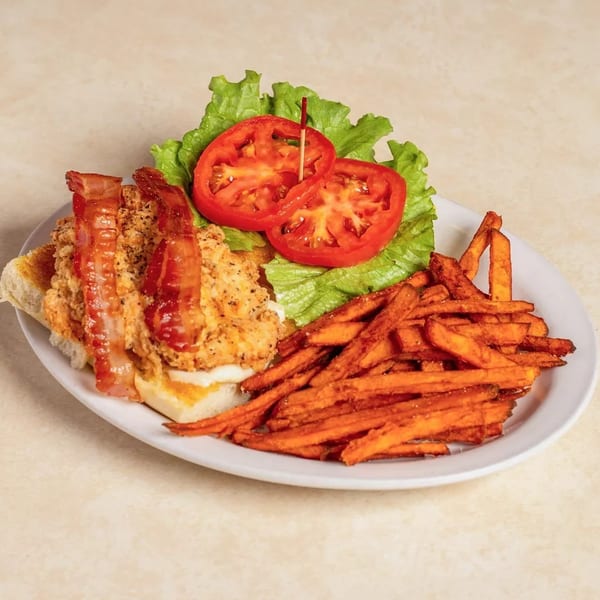 Chicken sandwich with bacon, lettuce, and tomato, served with a side of sweet potato fries.