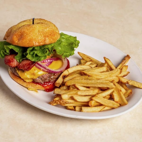 A cheeseburger with bacon, red onion, lettuce, and ketchup, served with a side of fries.