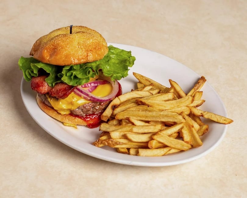 A cheeseburger with bacon, red onion, lettuce, and ketchup, served with a side of fries.