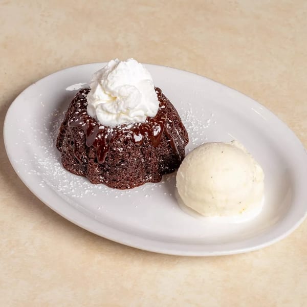 Chocolate lava cake with whipped cream, chocolate drizzle, powdered sugar, and a scoop of vanilla ice cream.