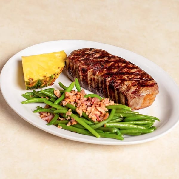 Grilled steak, green beans with bacon bits, and a pineapple wedge on a white plate.
